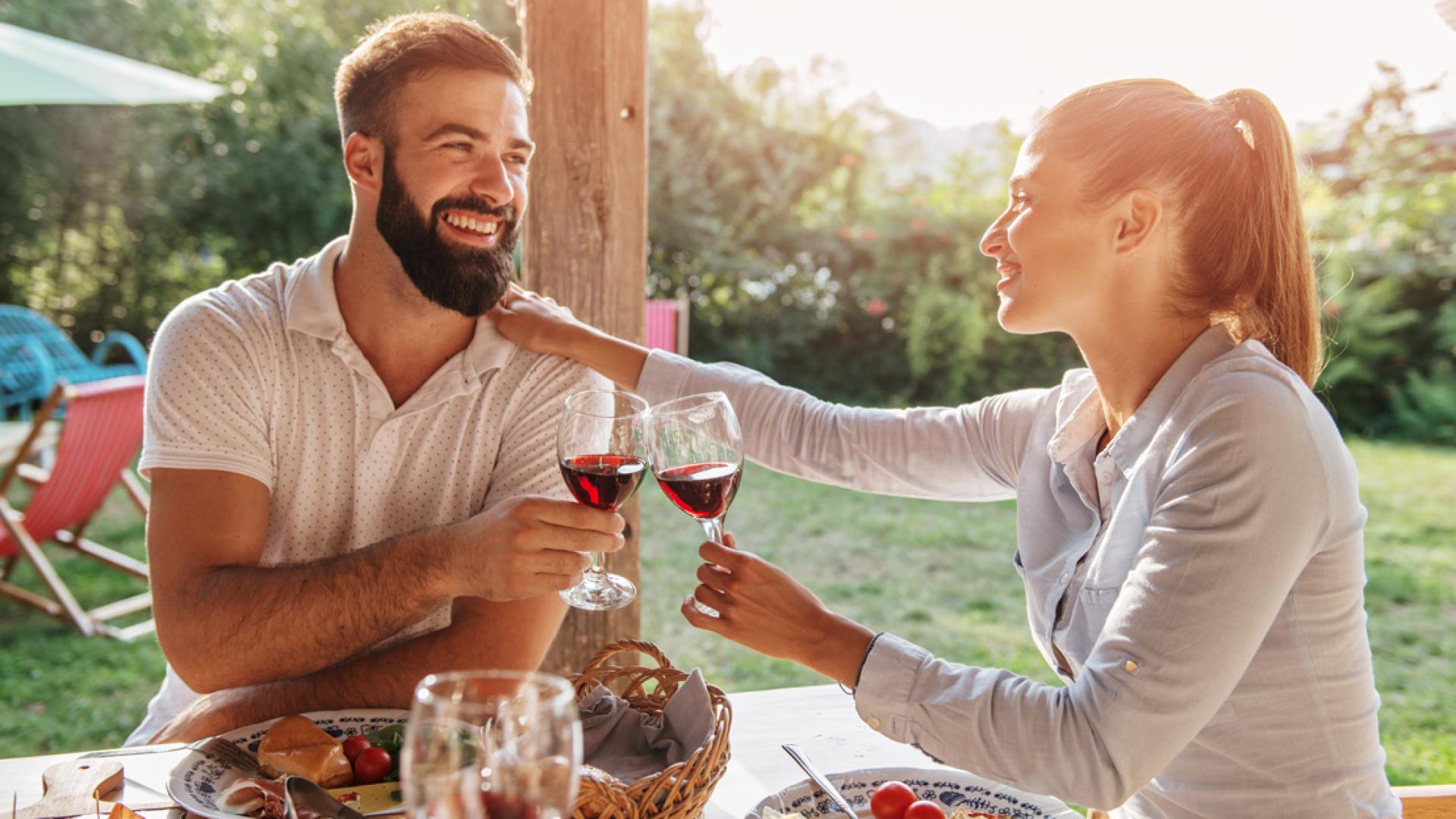 Coppia brinda con vino rosso durante un pasto all'aperto in una giornata soleggiata.