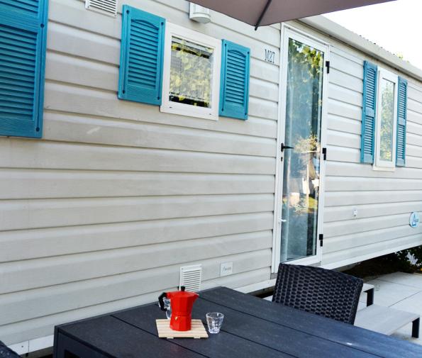 Mobile home with outdoor table, red coffee maker, and windows with blue shutters.