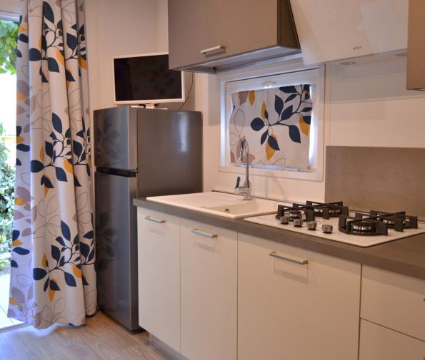 Modern kitchen with fridge, sink, stove, and leaf-patterned curtains.