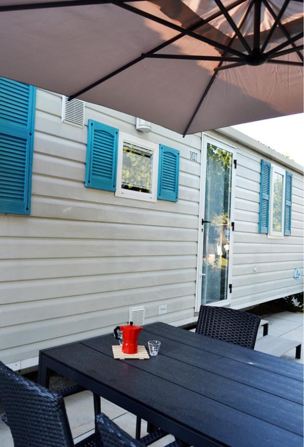 Outdoor table with coffee maker, umbrella, and caravan with blue shutters.